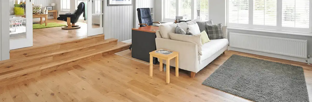 A modern living room with professionally installed laminate flooring, a beige sofa, a small side table, a gray rug, and large windows with white shutters in Aurora, CO